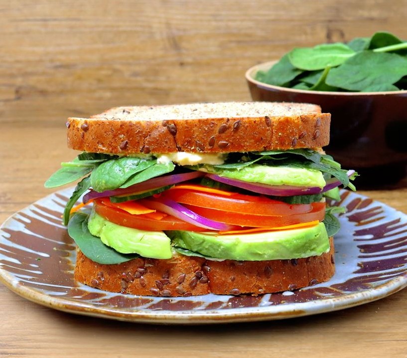 Close up image of a sandwich made with Country Harvest Grains+ Energy topped with avocado, tomatoes, hummus and spinach